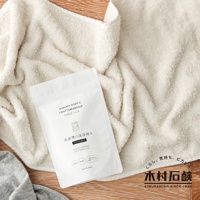 白色夾鏈袋裝的洗衣槽清潔粉，上面印有品牌名稱 KIMURA SOAP'S CRAFTSMANSHIP SINCE 1924。產品標示日文「洗槽槽的洗淨劑A」及英文「WASHING POWDER A FOR WASHING TUB」。產品置於淺米色毛巾上，背景為木紋桌面。