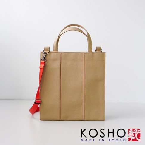 米色棉帆布手提托特包，帶有橙色縫線和可拆卸的鮮橙色肩帶，包身設計簡潔，有兩個提把。