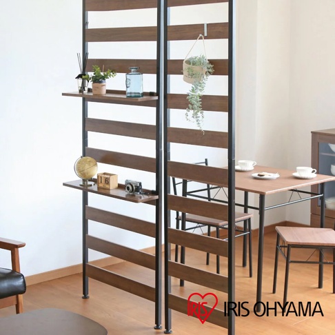 頂天立地收納掛架，深棕色木紋層板與黑色金屬支架，附有兩層置物台，左側層板擺放裝飾品，右側掛有綠植，後方為餐桌椅。