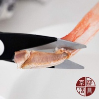 不鏽鋼萬用料理剪刀正在剪切一塊蟹腳，剪刀刀刃為銀色金屬，手柄為黑色。