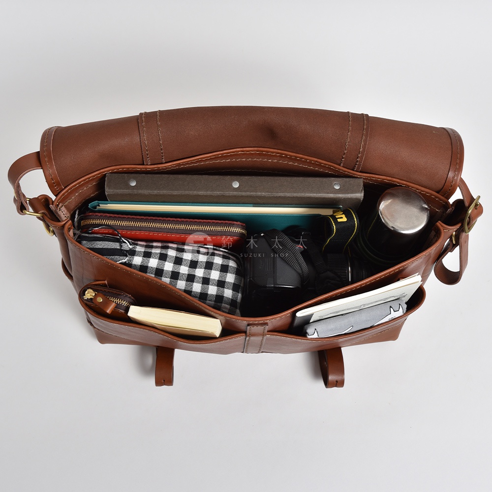棕色皮革復古郵差包，包內裝有書本、紅色長夾、黑白格紋布包、相機、金屬保溫瓶及筆記本。