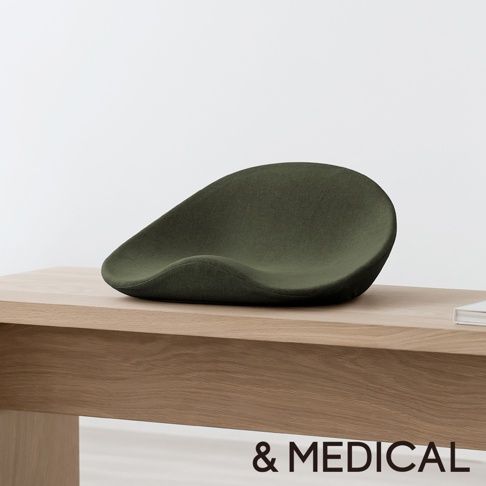 深綠色舒腰正姿座墊，採用布料材質，呈現人體工學曲線，置於木紋桌面上。