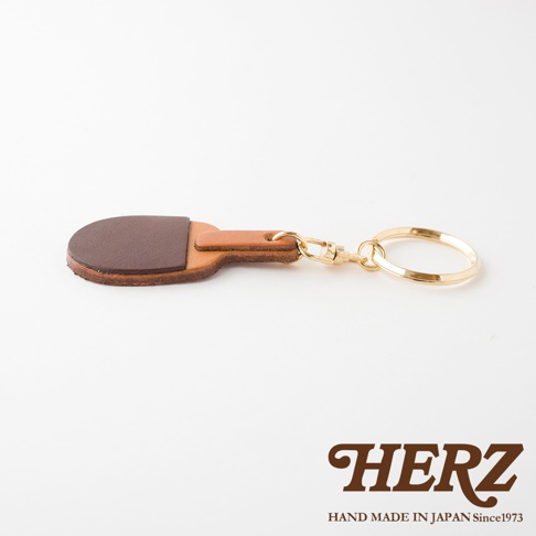 職人手作皮革桌球拍造型鑰匙圈，由兩種深淺不同的棕色皮革製成，搭配金色金屬掛環與扣環。