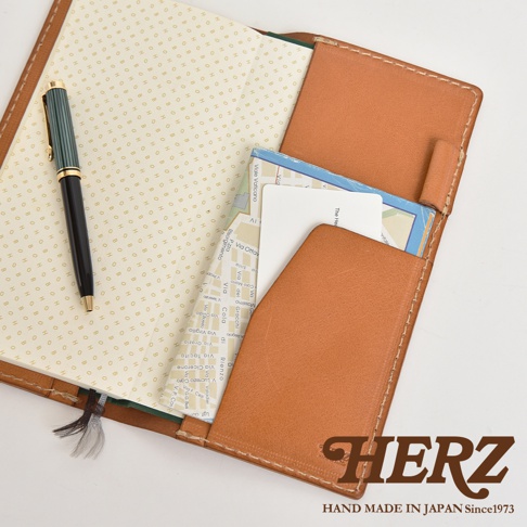 職人手作皮革旅行記事本書套，淺棕色皮革，內含筆、地圖與卡片，書套內頁印有細小的金色圓形圖案。