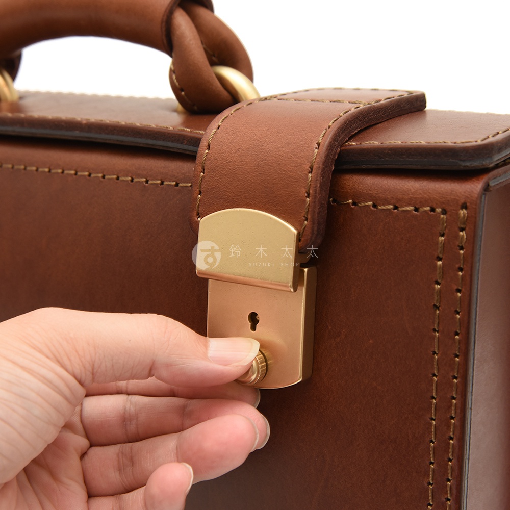 職人手作皮革機師箱 BC-31，採用棕色皮革製成，配有金色金屬鎖扣及手把。箱體邊緣有精緻的縫線裝飾，展現皮革的質感與工藝。