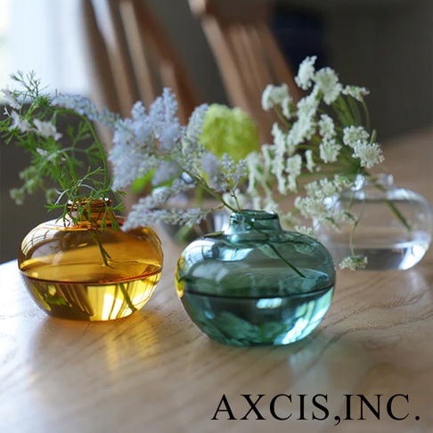 AXCIS,INC. 的 Lua 多功能線香玻璃花器，以琥珀色和綠色玻璃製成，上面插著細緻的白色花朵，呈現溫馨的氛圍。