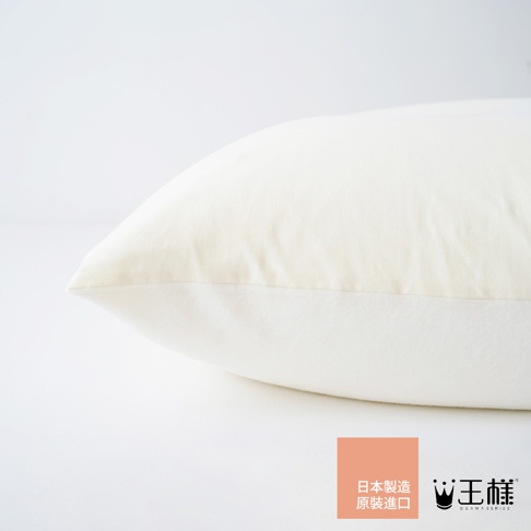 一張米白色枕頭的局部特寫，枕頭呈現飽滿的圓潤曲線，表面材質光滑，在右下角有一個標有「日本製造 原裝進口」的橘色方形貼紙，以及「王樣」的品牌標誌。
