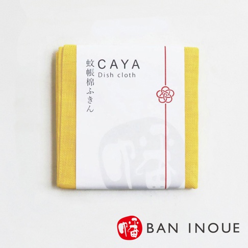 黃色蚊帳布拭巾，邊緣為細緻織紋，包裹著白色品牌標籤，標籤上有日文「蚊帳棉ふきん」和英文「Dish cloth」字樣，以及紅色繩線與梅花圖案。
