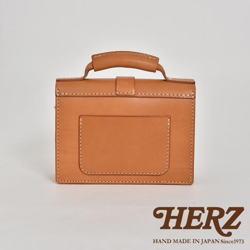 職人手作的經典混合風迷你單肩包，採用天然皮革材質，呈現溫潤的棕褐色。包款設計簡潔，帶有手提把和外部收納袋，縫線精緻，展現高品質的工藝。