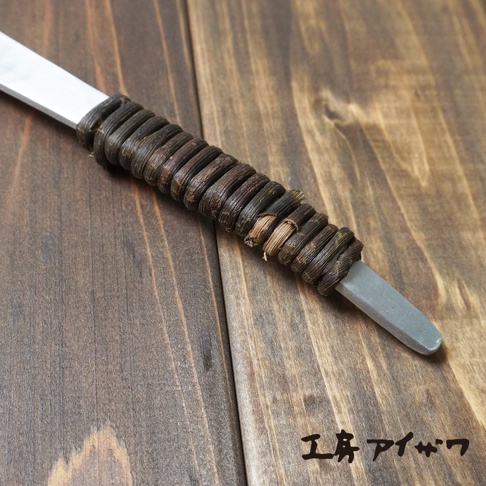 鋁製湯勺，勺柄部分纏繞著深棕色繩索，表面有錘目紋，置於木紋背景上。