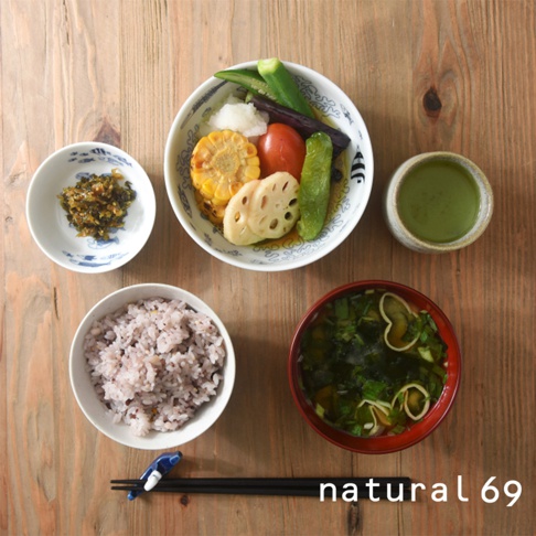 一碗紫米飯，一碗裝有玉米、蓮藕、番茄、秋葵、茄子和蘿蔔絲的蔬菜雜燴，一碗味噌湯，一小碟醃漬物，以及一杯抹茶，整體擺放在木紋桌面上。