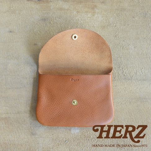 職人手作的棕色皮革小物收納袋，掀蓋式設計，附有金屬鈕扣。袋面壓印「Organ」字樣，材質呈現皮革自然紋理。