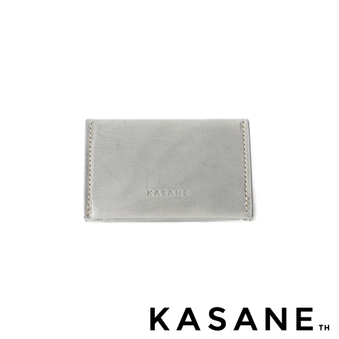 KASANE 職人手作義大利 Sibilla 皮革卡片收納夾，呈現淺灰色皮革的細膩質感，右側邊緣有縫線細節，正面中央壓印 KASANE Logo。