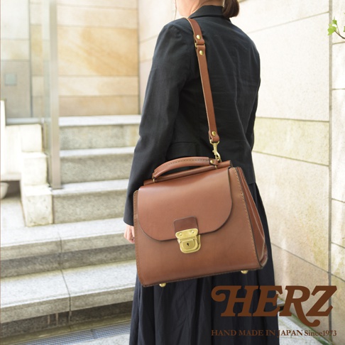 一手提、斜背兩用的棕色皮革公事包，上面有金屬鎖扣及品牌 logo。