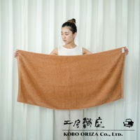 一位女性手持一條淺棕色人字紋有機棉浴巾，浴巾紋理清晰。