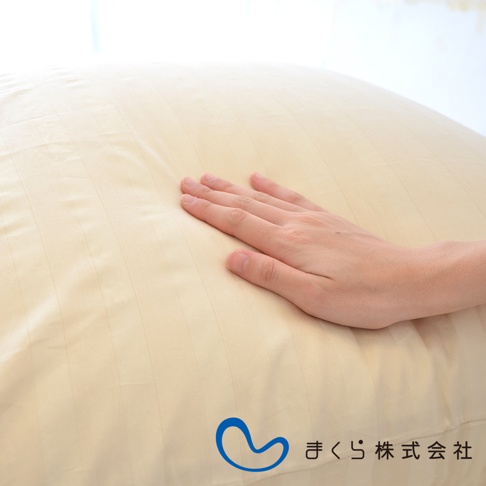 淺米色條紋枕套，布料光滑，一隻手輕柔按壓在枕套上，展示其柔軟觸感。