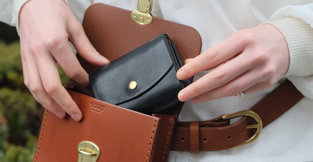 職人手作皮革經典腰包 E-1，展示一個棕色皮革腰包，內裝一個黑色皮革短夾，腰包和短夾皆配有金色金屬扣。