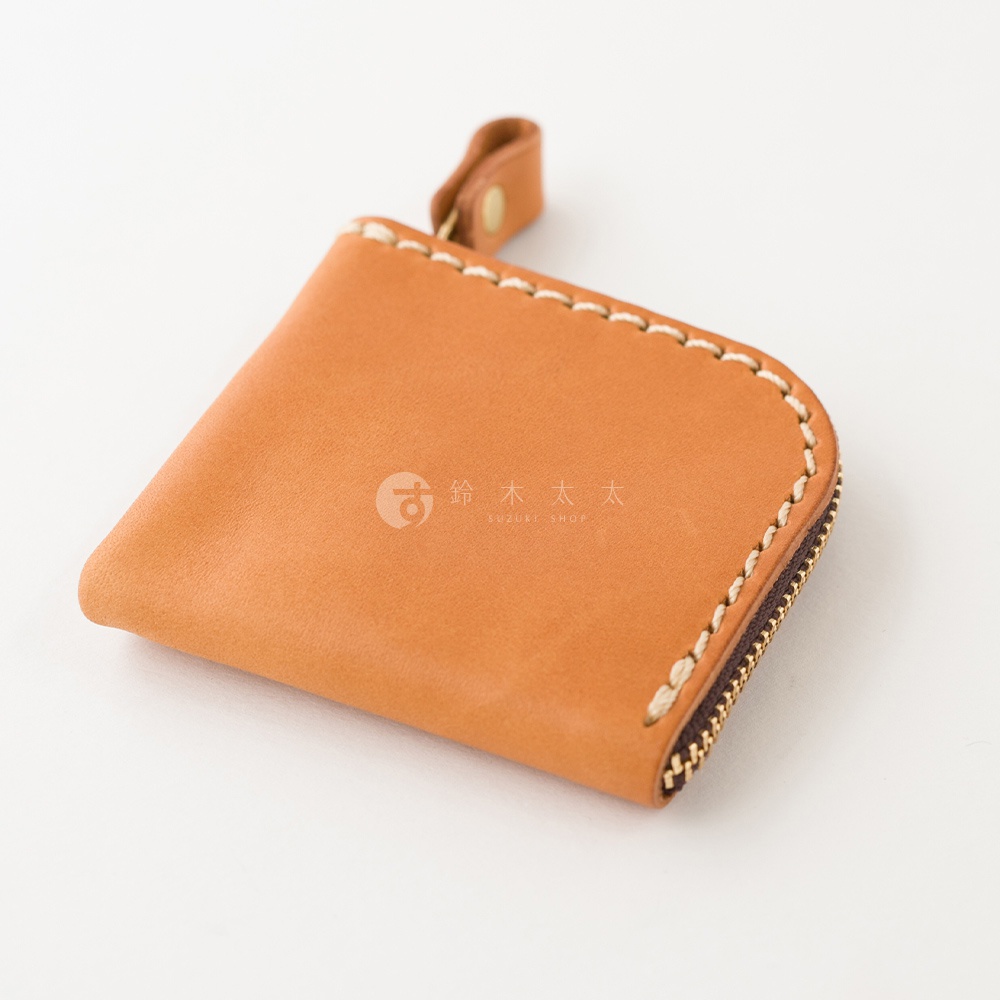 日本HERZ職人手作淺棕色皮革零錢包，外觀呈現簡約的正方形設計，邊緣以粗線手工縫製，側面搭配金屬拉鍊與皮革拉環，包身中央印有鈴木太太商標，展現細緻的皮革質感。