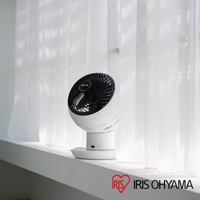 白色圓形機身的 IRIS OHYAMA 空氣循環扇，黑色扇網，放置在白色窗簾前的窗台上。
