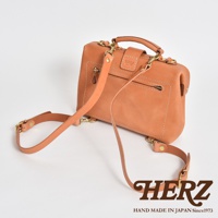 皮革迷你軟皮杜勒斯包，淺棕色，配有可拆卸肩帶和金色金屬配件，正面有一個拉鍊口袋和品牌標誌。