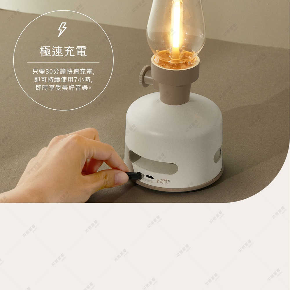 淺米色煤油燈造型藍牙音響，帶有透明燈罩和黃色LED燈泡，側面有灰色旋鈕和USB Type-C充電孔，一隻手正將充電線插入孔中。