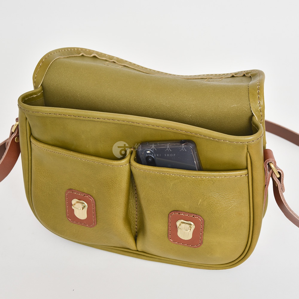橄欖綠皮革傳統釣魚包，配有兩個前袋，一個裝有手機，兩個帶有金屬扣的棕色皮革裝飾。
