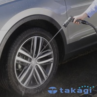 銀色汽車的輪胎和車身側面，手持灰色噴水槍噴灑水柱，水花濺射在車輪上。