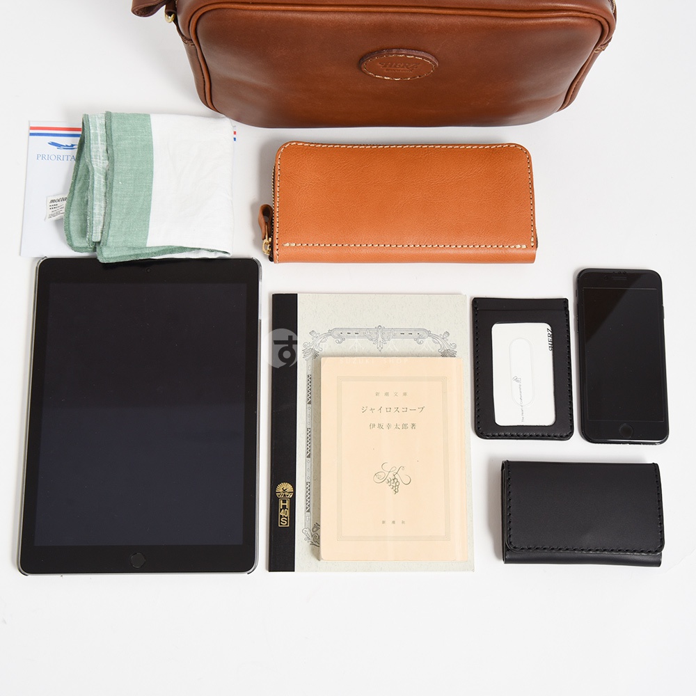 皮革手提包、橘色長夾、黑色手機、黑色卡夾、黑色皮夾、平板電腦、綠色毛巾和一本日文書。
