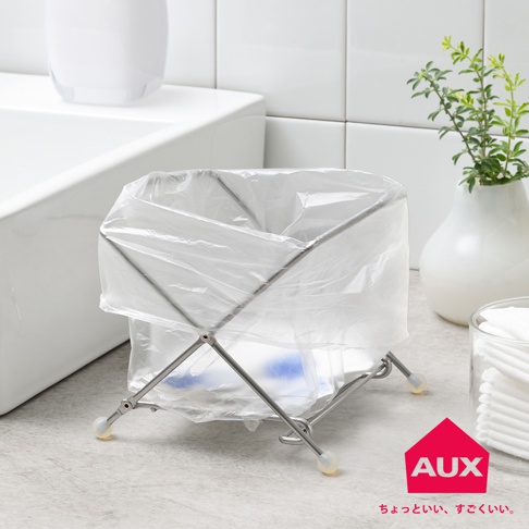 銀色金屬支架，配透明塑膠垃圾袋，支架結構為可折疊的 X 型，底部有四個圓形塑膠腳墊，整體置於淺色檯面上。