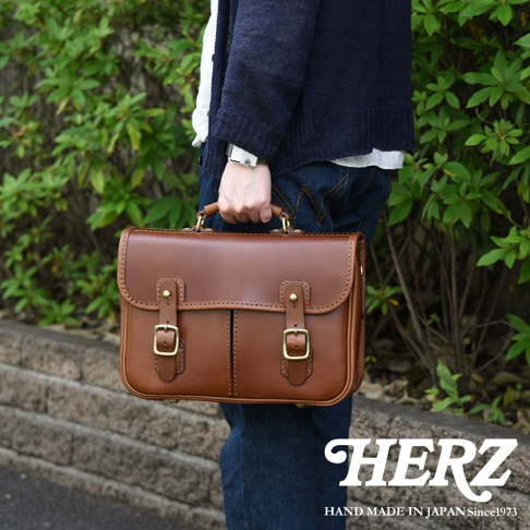 職人手作棕色皮革兩用單肩包，帶有翻蓋、兩個皮帶扣和頂部提把。