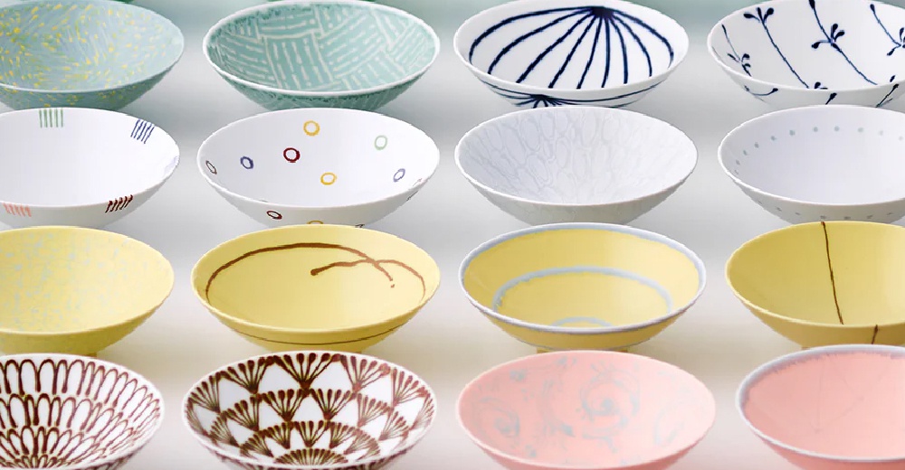 展示多款陶瓷平茶碗，有淺藍色帶綠色線條、白色帶彩色圓點、白色帶黑色放射狀線條、白色帶藍色樹枝圖案、淡黃色帶棕色線條、淡黃色帶藍色圓圈、粉紅色帶淺色花紋等不同設計。