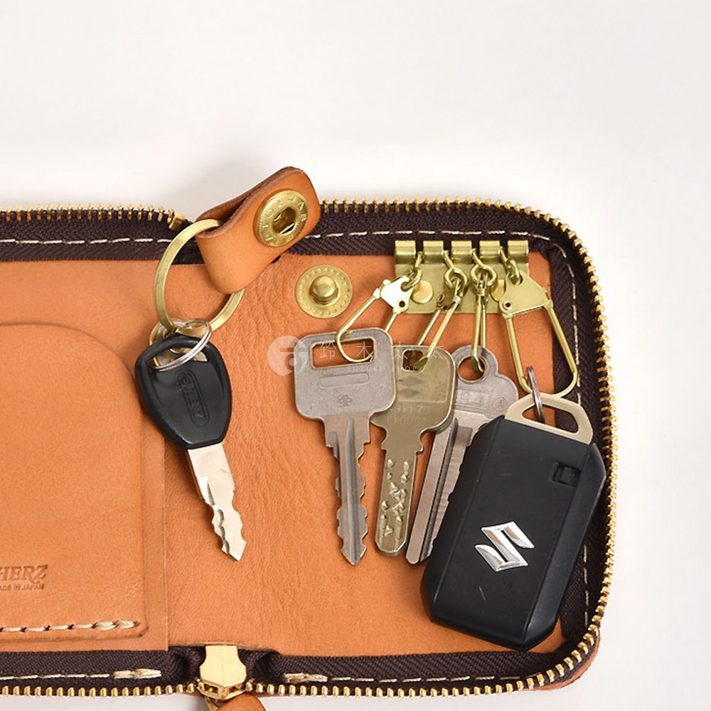 職人手作皮革多用途收納鑰匙包，淺棕色皮革內襯，設有四個金色鑰匙掛鉤，一個黑色汽車遙控器及數把金屬鑰匙。