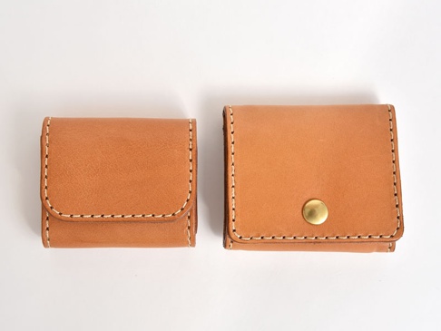 兩個棕褐色皮革製的雙折收納零錢包，其中較大的零錢包有一個金色圓形按扣。兩個零錢包均以白色縫線手工製作，邊緣圓潤。