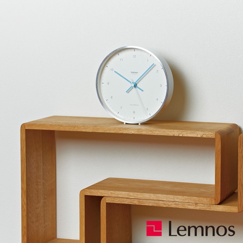 Mizuiro時鐘，白色圓形錶盤，銀色金屬邊框，藍色時針、分針和秒針，錶盤上標有黑色數字和刻度。時鐘放置在木質層架上。