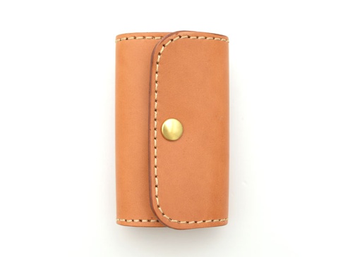 淺棕色皮革製作的六鉤鑰匙包，採用經典的閉合設計，配有金色金屬按扣，車縫線清晰，展現職人手作質感。