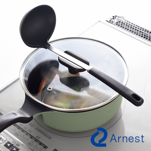 Arnest 鴛鴦鍋上放著湯勺，湯勺上有一個固定架，鍋子放在電磁爐上，鍋蓋透明，裡面有食材。
