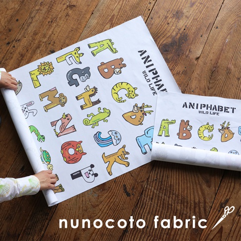 一張展開的白色無框帆布藝術海報，上面印有以動物夥伴組成的字母圖案，色彩鮮豔，包括獅子、熊、貓、鹿、大象、猴子、蜥蜴、無尾熊、水母、烏龜、熊貓等，字體為「ANIPHABET WILD LIFE」。