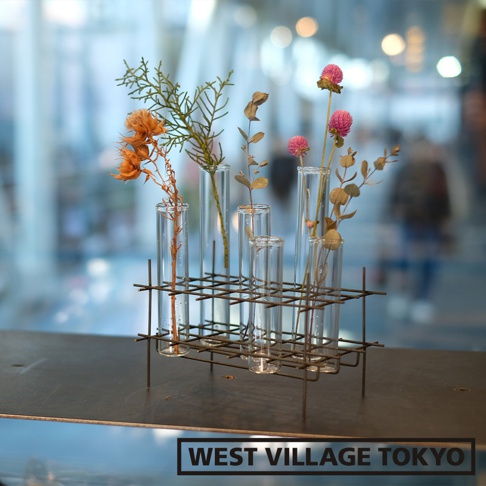 金屬網架上的多個玻璃試管花器，內插有乾燥的橘色花朵、綠色植物和粉紅色球狀花朵。