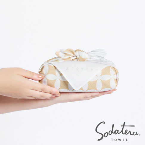 養育TOWEL 和緣紋樣風呂敷毛巾，由雙手捧著，上面裝飾著日式傳統花紋的布料和精緻的蝴蝶結。