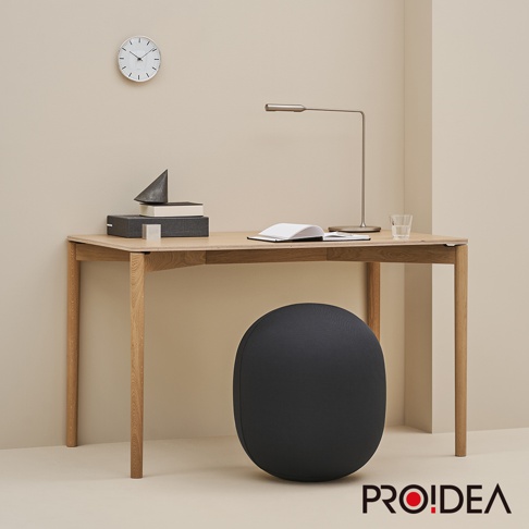 一個黑色的、橢圓形的收納彈力平衡球，置於木製書桌下方，球體表面為織物材質。