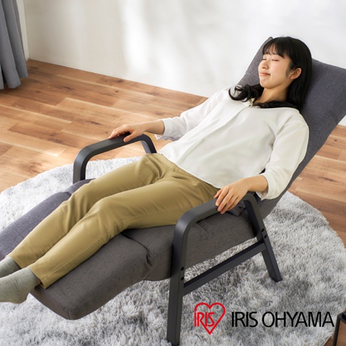 一位女性坐在深灰色布面、黑色金屬框架的躺椅上，扶手為木質。