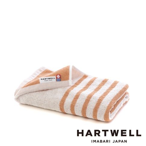 一條折疊的迷你浴巾，帶有橙色與白色的條紋，材質柔軟，左上角有一個印有「HARTWELL IMABARI JAPAN」的標籤。
