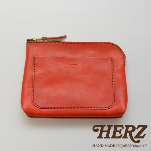 一個橘紅色的職人手作皮革小物收納包，有拉鍊封口和外部置物袋，縫線精緻，皮革質感佳。