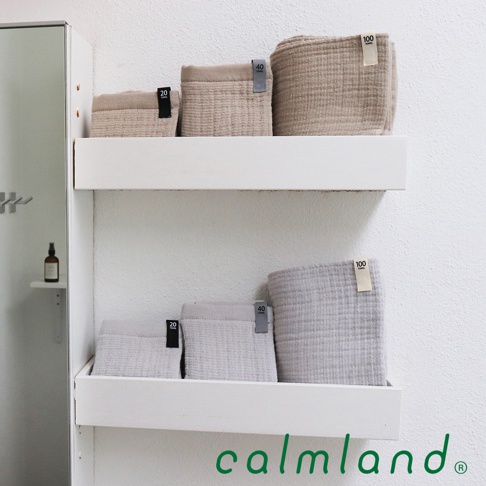 架上展示共六條毛巾，其中三條為淺褐色，三條為淺灰色。毛巾質地看起來柔軟，帶有明顯的紋理。部分毛巾上有標示尺寸的黑色標籤，分別標有「20」、「40」和「100」。