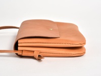 職人手作皮革橫式隨行袋 (CP-9)，採用天然皮革材質，呈現柔和的淺棕色。袋子設計簡潔，以側邊視角呈現，可見其厚實的皮革層疊，並配有細長的皮革背帶，背帶與袋身以皮革繩結固定。