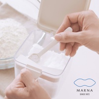 透明塑膠製的調味料盒，附有白色勺子，正在舀取白色顆粒狀的調味料。盒子設計簡潔，有白色密封蓋和卡扣。