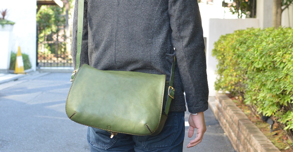職人手作復古翻蓋郵差包，採用綠色皮革製成，配有可調節肩帶和金色金屬扣，風格簡約。