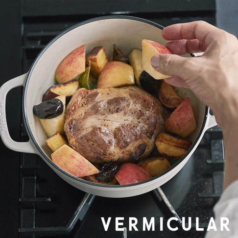 琺瑯鑄鐵鍋 OP2 18cm，內有烤雞腿肉、切塊的蘋果和李子，鍋子為白色，手正在放入蘋果塊。