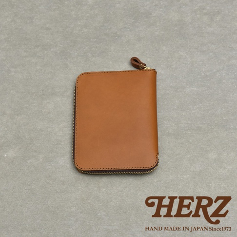 HERZ 品牌標誌，下方為 HAND MADE IN JAPAN Since1973 字樣，圖片中央為一個棕色皮革拉鍊收納包。