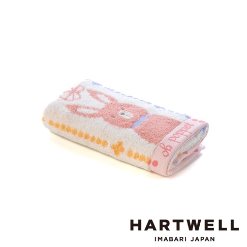 這是一條摺疊起來的 HARTWELL 今治森林動物刺繡毛巾，毛巾以柔和的米白色為底色，表面印有可愛的粉色兔子圖案與橘黃色點狀裝飾，邊緣綴有 poppet 的英文刺繡，整體呈現出溫馨精緻的日式風格。